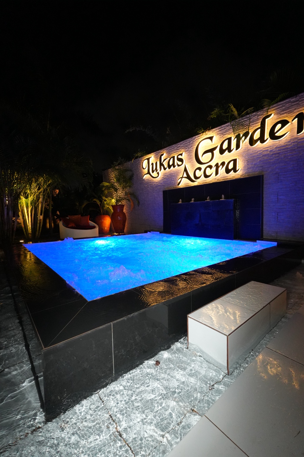 Illuminated jacuzzi pool at night below the lit Lukas Garden Accra sign