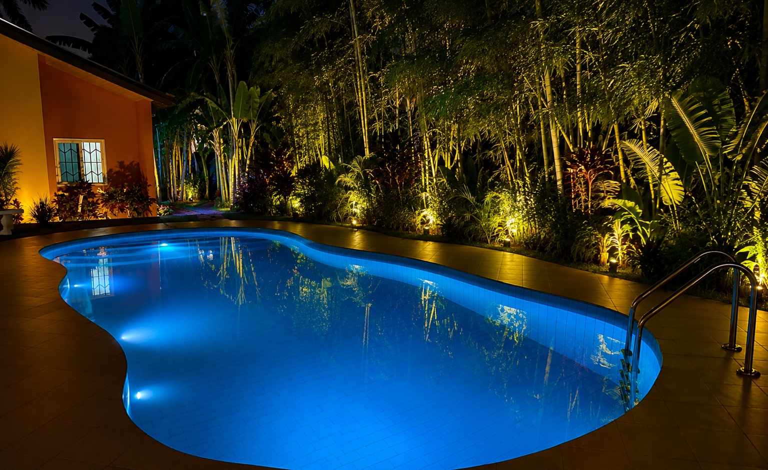 Main pool glowing blue at night beside a lit bamboo garden