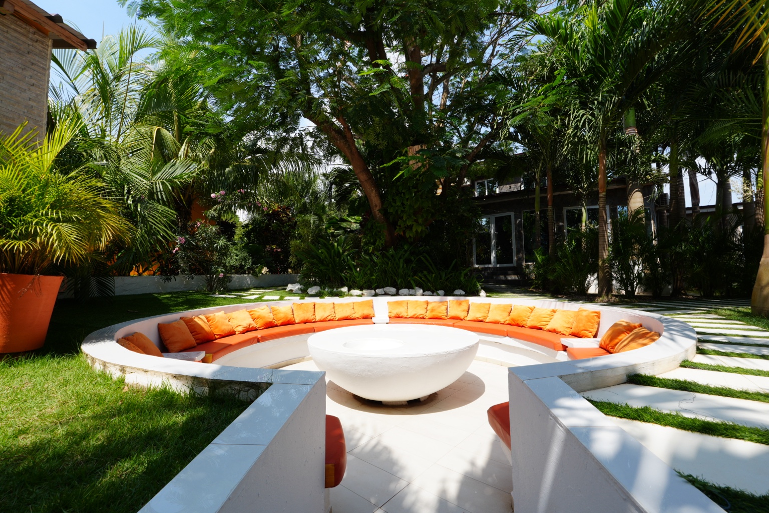 Circular sunken lounge with orange cushions in the sunlit tropical garden